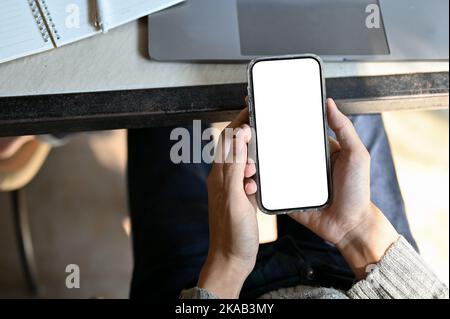 Top view image, A male hands holding a smartphone white screen mockup at his office desk. Stock Photo