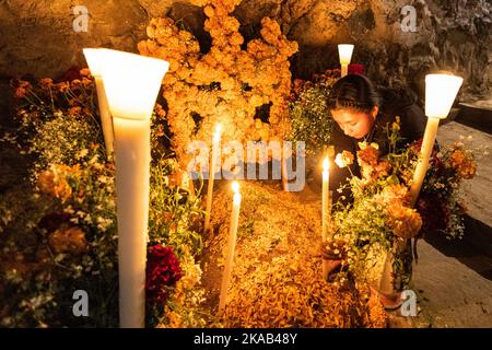 Morelia, Mexico, 1 Nov 2022, A Purepecha girls steadies a candle during the Day of the Dead celebration in the cemetery of Arocutin, Michoacan, Mexico. The indigenous Purepecha of this village prepare this annual ritual of remembrance by constructing altars with marigolds, candles and the favorite food or drink of the deceased.  The vigil takes place the night of November 1st and has become a major tourist attraction in the central Mexican state of Michoacan.  Brian Overcast/Alamy Live News Stock Photo