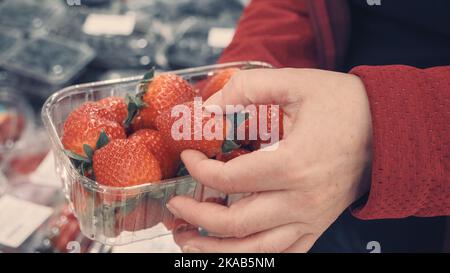 Woman choose fresh strawberries in a shop. Shot close up of berries and hands Stock Photo