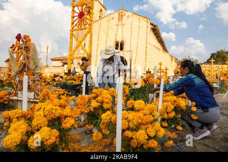 Morelia, Mexico, 1 Nov 2022, A couple puts finishing touches on an altar during the Day of the Dead celebration in the cemetery of Arocutin, Michoacan, Mexico. The indigenous Purepecha of this village prepare this annual ritual of remembrance by constructing altars with marigolds, candles and the favorite food or drink of the deceased.  The vigil takes place the night of November 1st and has become a major tourist attraction in the central Mexican state of Michoacan.  Brian Overcast/Alamy Live News Stock Photo