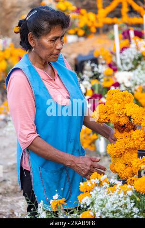 Morelia, Mexico, 1 Nov 2022, A Purepecha woman arranges marigold flowers during the Day of the Dead celebration in the cemetery of Arocutin, Michoacan, Mexico. The indigenous Purepecha of this village prepare this annual ritual of remembrance by constructing altars with marigolds, candles and the favorite food or drink of the deceased.  The vigil takes place the night of November 1st and has become a major tourist attraction in the central Mexican state of Michoacan.  Brian Overcast/Alamy Live News Stock Photo