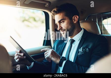 Email check before I get in. a handsome young corporate businessman using a tablet while commuting. Stock Photo
