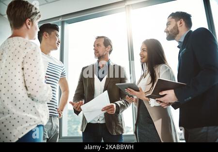 Who will be taking this one on. a group of focused business people working together on ideas while standing in the office during the day. Stock Photo