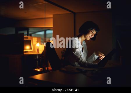 Getting it done before the day is gone. a young businesswoman using a digital tablet during a late night at work. Stock Photo