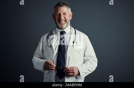 I find fulfilment in saving lives. Studio shot of a handsome mature male doctor looking thoughtful while standing against a dark background. Stock Photo