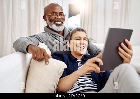Nowadays this is the best way to spend our days. an affectionate senior couple using a tablet while relaxing on the sofa at home. Stock Photo