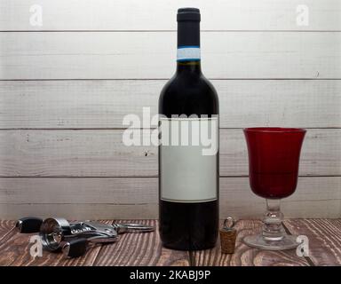 Bottle of red wine with blank label, corkscrew and red glass. Stock Photo
