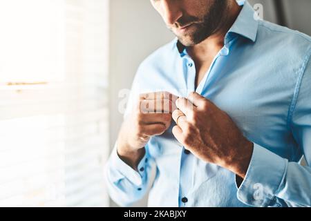 Have to button up my shirt. an unrecognizable man buttoning up his shirt in his bedroom at home. Stock Photo