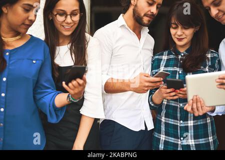 Communicating in all forms. a group of young creative businesspeople using mobile devices while talking to each other. Stock Photo