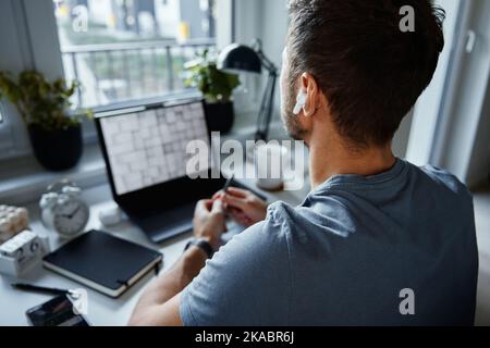 Home office workplace with laptop. Man working remotely from home, using laptop. Male freelancer sitting at table near window Stock Photo