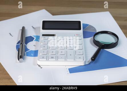 Calculator, magnifying lens on business paper documents withblue charts and graphs. Stock Photo