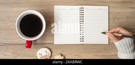 Woman hand writing on notebook with black coffee cup and Christmas cookies on table. Xmas, Happy New Year, Goals, Resolution, To do list, Strategy and Stock Photo