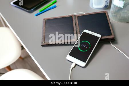 Mobile phone charging with portable solar panel over office desk Stock Photo