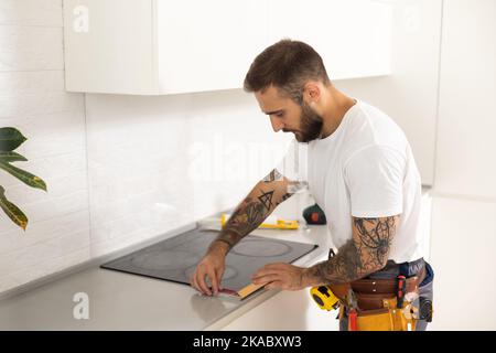 craftsman installs hob in kitchen. Household Appliance Installation Services Concept Stock Photo