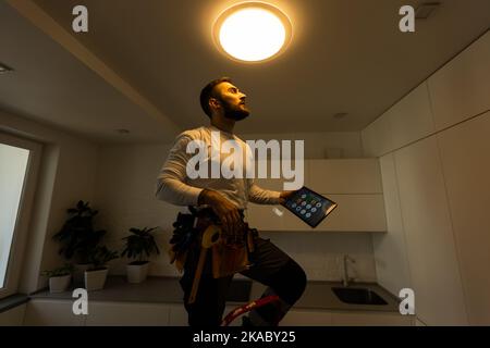 Installation lighting. Builder is holding a tablet in his hands. Concept - lighting engineer. Process installing. Electrician Stock Photo