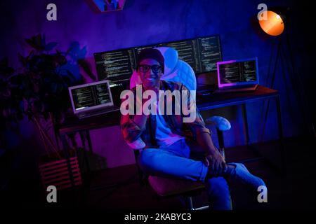 Photo of positive intelligent hacker sitting chair hand touch chin server operating evening loft room indoors Stock Photo