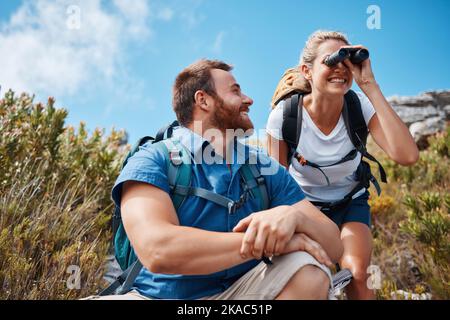 Woman hiking, using binoculars and couple adventure happy together with smile in nature on travel. Mountain man, backpack girl happiness and outdoor Stock Photo