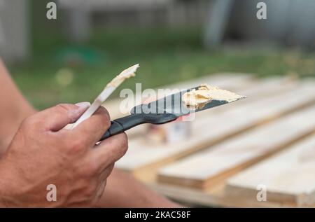 Putty on spatula tool in male hands closeup, repairing wood with paste. Stock Photo
