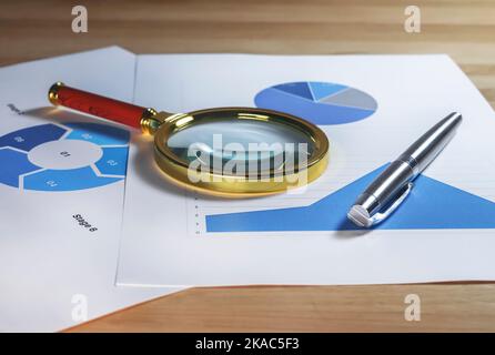 Magnifying lens on documents with business charts and graphs. Stock Photo
