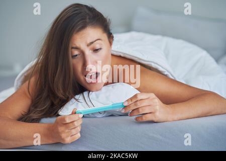 Young brunette woman with pregnancy test in the bed Stock Photo