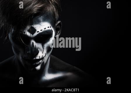 Halloween costume. Man with skeleton make-up. The man looks into the camera. Dark background. Stock Photo