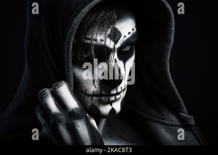 Halloween costume. Man with skeleton make-up. The man looks into the camera. Dark background. Stock Photo