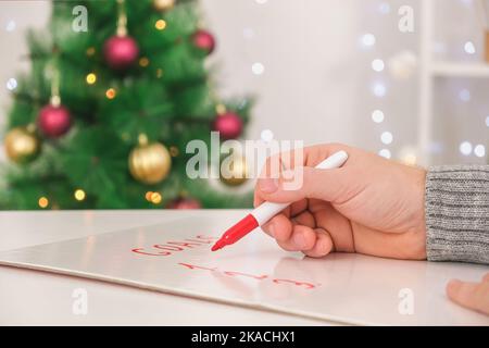 A man writes marker board white table with Christmas decor goals and plans for the new year and Christmas. Goals for the new year written on a marker board. Wishes and goals for the new year 2023. Stock Photo