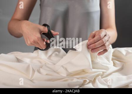 Female hands closeup cutting pastel cloth with sewing scissors. Dressmaker at work process. Stock Photo