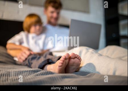 Ginger man and his cute son lying in bed with their gadgets Stock Photo