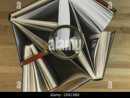 Magnifying glass over books on wood table, top view. Reading and studying concept. Stock Photo