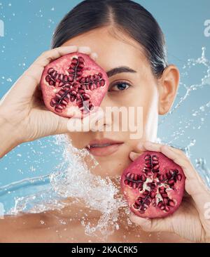 Face, skincare and pomegranate in woman hands with water splash for facial organic, eco friendly or vegan product in studio blue mock up. Model with Stock Photo