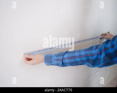 Side view of serious man using measuring tape in room with underfloor heating pipes. Designer in shirt taking measurements while working on renovation of apartment. Stock Photo