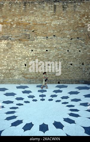 One Woman Walks or Walking Across Decorative Pavement, Pedestrian Area or Town Square in Grignan Drôme Provence France Stock Photo