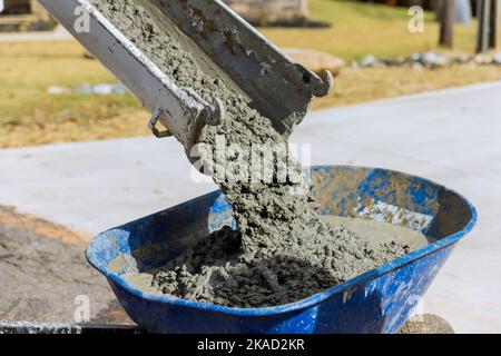 Concrete mixer truck pouring wet cement into blue wheelbarrow in construction site Stock Photo