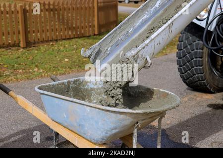 In construction site concrete mixer truck is pouring wet cement into wheelbarrow Stock Photo