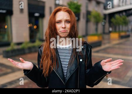 Portrait of distraught young woman with long red-hair standing with wet, disheveled hair after being caught in cold autumn rain, crying looking at Stock Photo