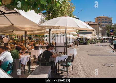 Italy food drink, view in summer of people lunching on restaurant terraces along the eastern edge of Lake Como in the city of Como, Lombardy, Italy Stock Photo
