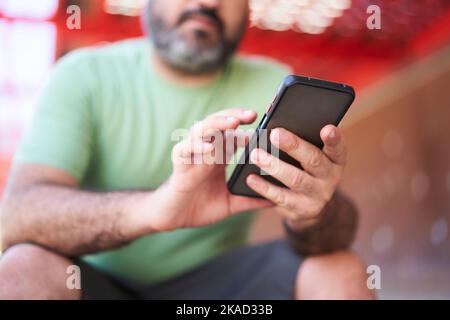 Close-up of unrecognizable man using phone outdoors. Focus on cell. Using mobile to check his bets. Stock Photo