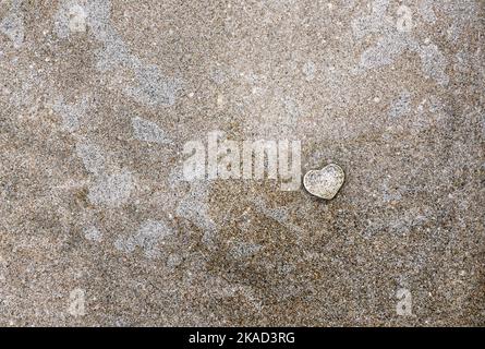 Small clear glass heart on beach sand with thin layer of water. Stock Photo