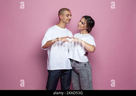 Cheerful young man and pretty young woman making heart together on pink background Stock Photo