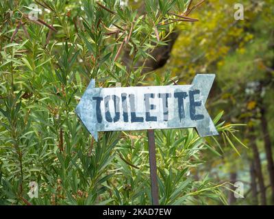 Sign in a park with the inscription toilets. A sign with an arrow pointing to the left. Blurred background. Stock Photo