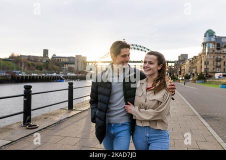 A wide-view shot of a young couple walking side by side together, they are in love. Stock Photo