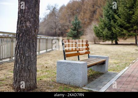 A beautiful view of a wooden bench in a park next to a tree in China Stock Photo