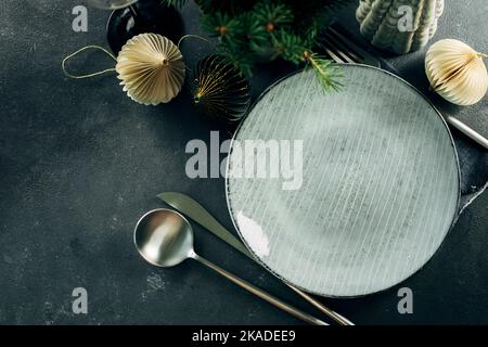 Christmas table setting with empty craft ceramic plate and silver cutlery on dark stone background. Top view, copy space Stock Photo