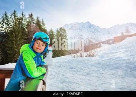 Boy stand at balcony, smile in ski outfit glasses and helmet Stock Photo