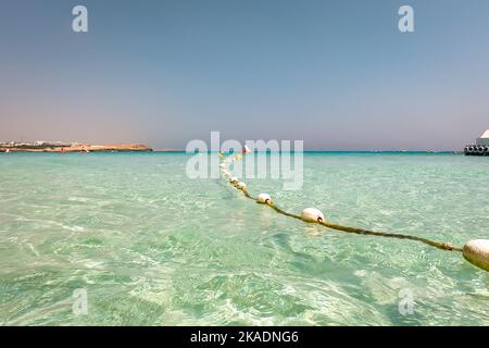 String of white marker buoys floating in the sea, watersport boats on background. Turquoise water and golden sand at Nissi beach, Cyprus. Stock Photo