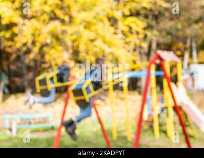 Defocused image of bright yellow foliage on playground on sunny autumn day in park Stock Photo
