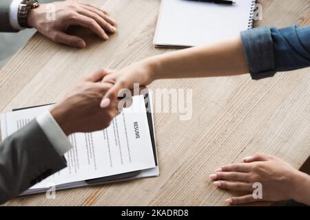 Cropped view of resume near blurred businessman and woman shaking hands during job interview,stock image Stock Photo