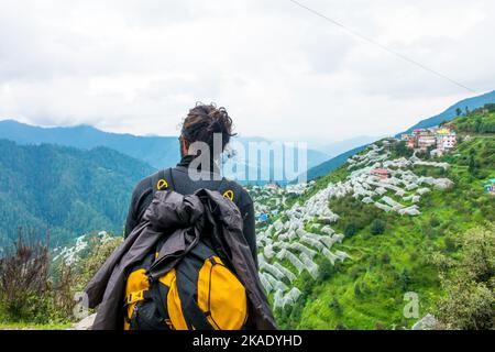 July 19th 2022 Himachal Pradesh India. A male tourist with a backpack looking towards an apple orchid covered in anti hail nets in a valley at Shimla. Stock Photo