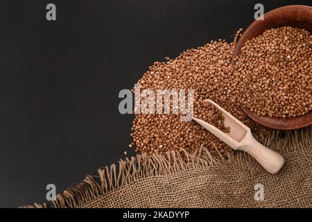 Raw buckwheat in a wooden spoon, in bulk and in a clay plate on a black table. Close-up. Selective focus Stock Photo